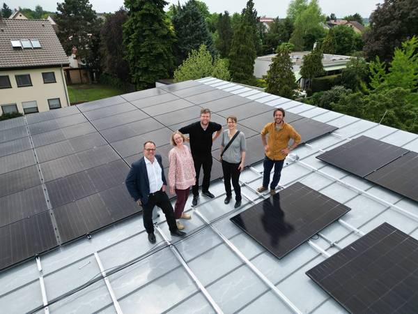 fünf Personen stehen auf einem Flachdach neben Solarmodulen