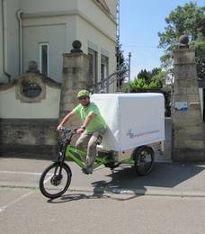 Person mit grünem T-Shirt fährt aus einem Eingang mit einem grünem Lastenrad heraus