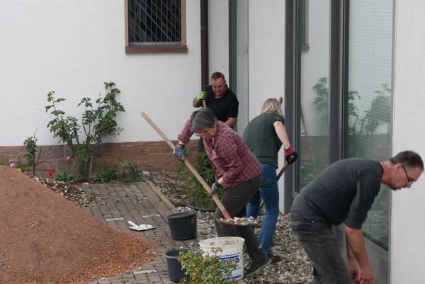 Quelle: Evang. Kirchengemeinde Malsch/U.Nell Menschen, die ein Beet anlegen an einem Haus, Schippen, Eimer, Kies und Bodensubstrat