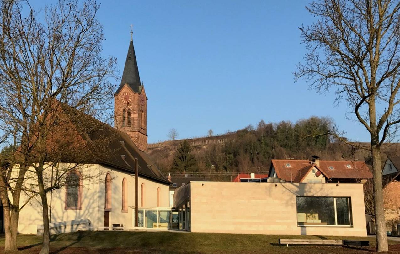 Foto der Kirche und des Gemeindehauses orange angestrahlt von der untergehenden Sonne