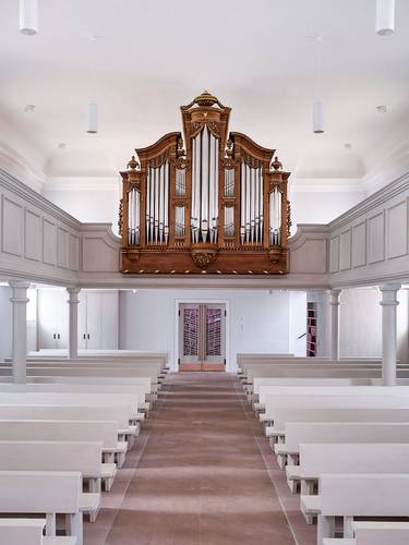 Blick über die hellen Bänke auf die Orgel über dem Eingang auf der Rückseite des Kirchenraums