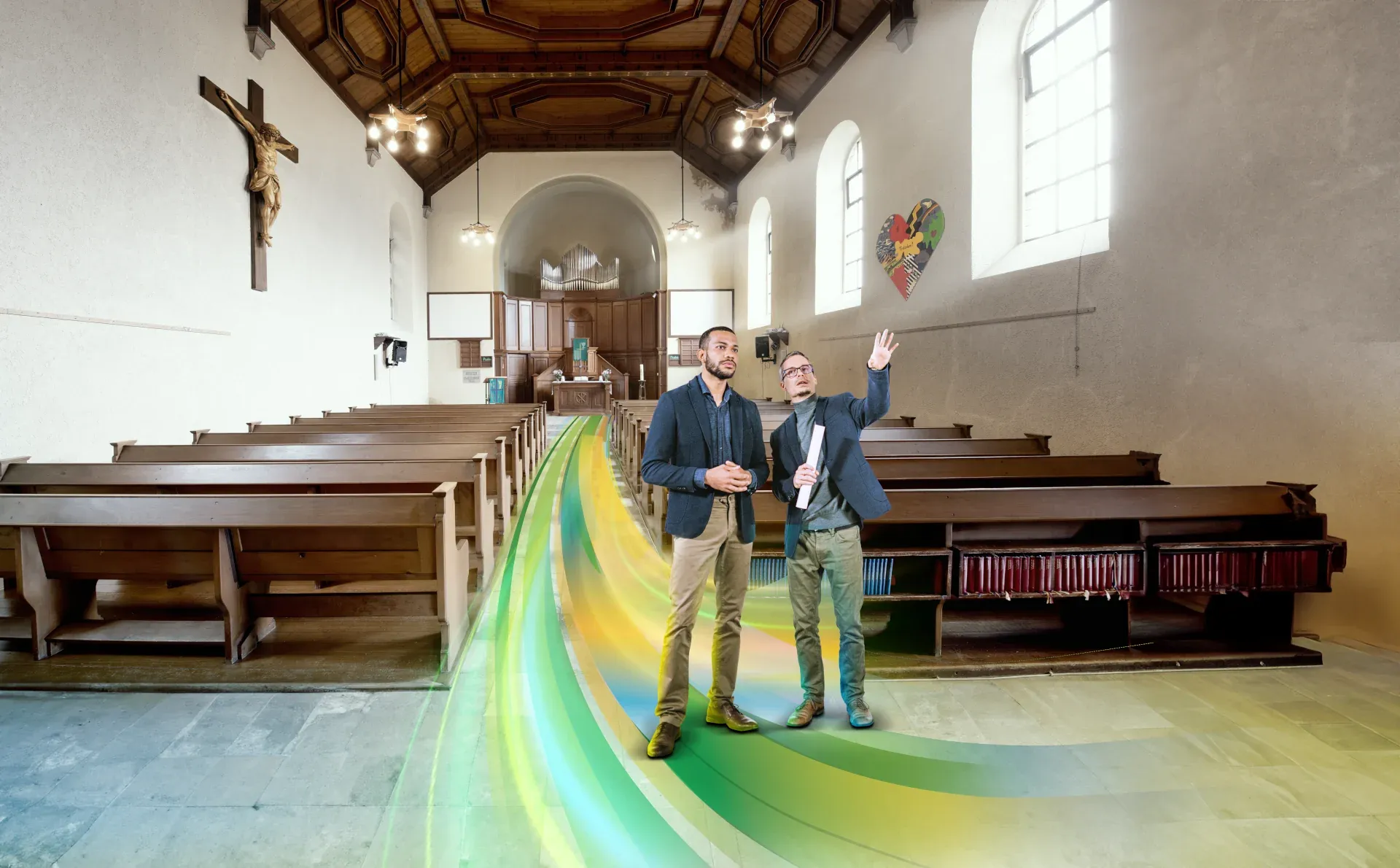 Der Innenraum der Bergkirche Schönau. Zwei Männer stehen auf einem farbigen Weg hinter der letzten Bankreihe und zeigen Richtung Empore.