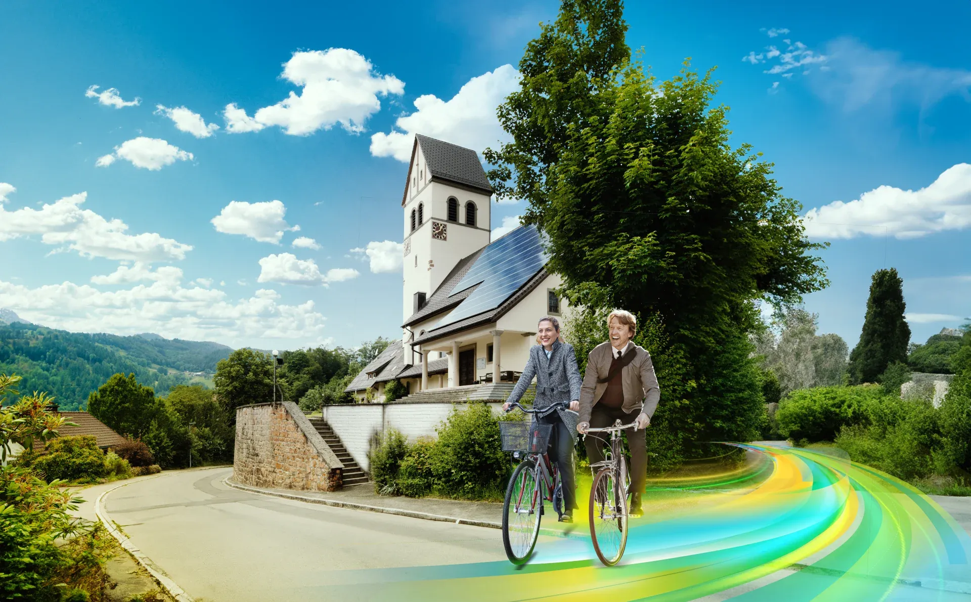 Ein Mann und eine Frau mit Fahrrädern fahren auf einem farbigen Weg zur Bergkirche Schönau.